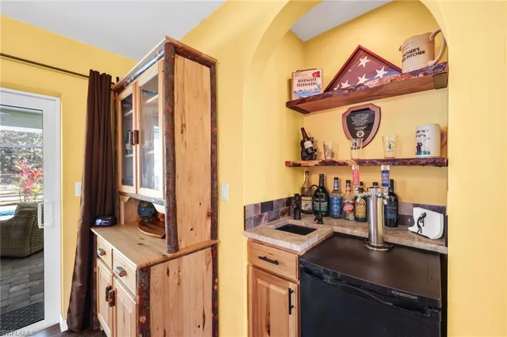 Indoor wet bar featuring open shelves, black dishwasher, glass insert cabinets, and light stone counters