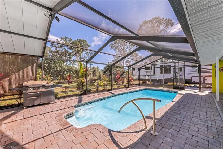 Outdoor pool featuring glass enclosure, a sunroom, a patio, and area for grilling