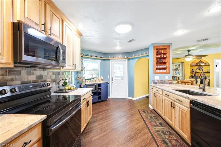 Kitchen with black appliances, light stone counters, arched walkways, and light brown cabinetry