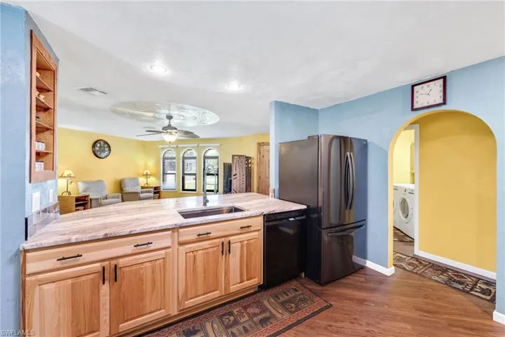 Kitchen featuring light brown cabinets, light stone countertops, open floor plan, dark wood-type flooring, and black dishwasher
