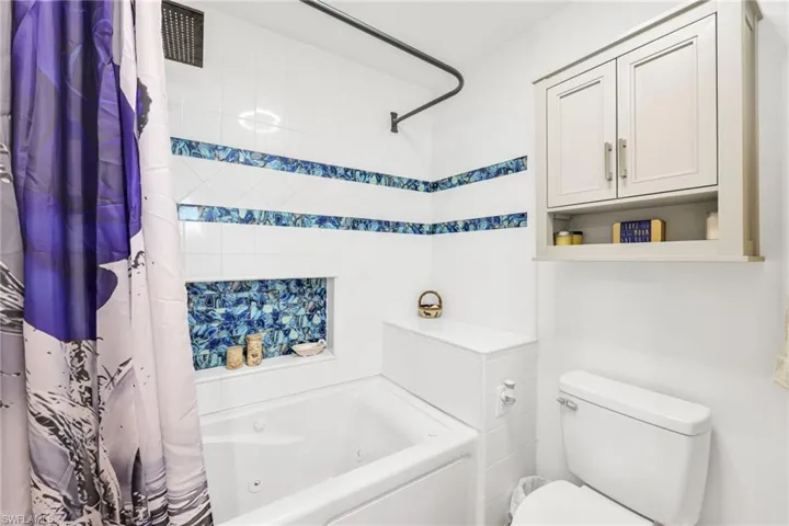 Bathroom featuring a combined bath / shower with jetted tub and toilet