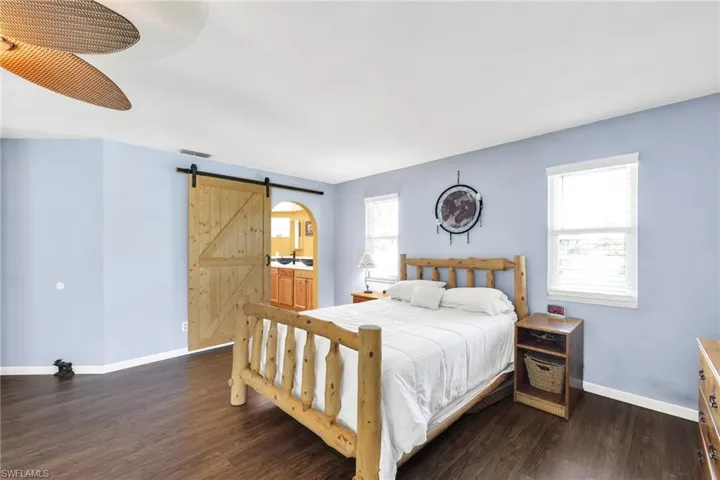Bedroom with a barn door, dark wood-style floors, ceiling fan, and ensuite bath