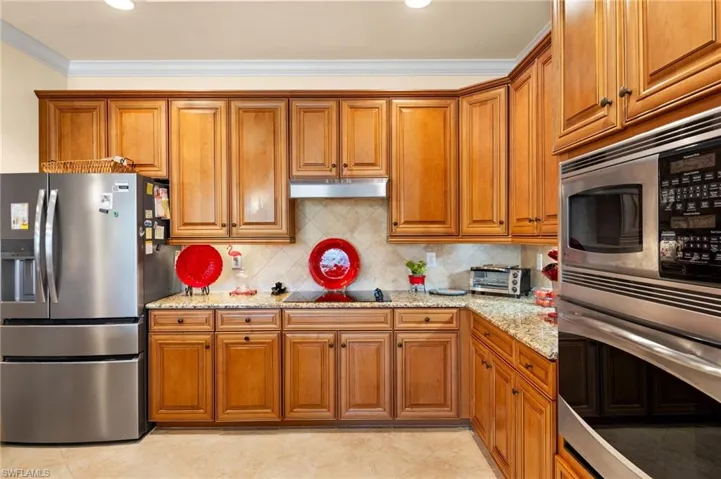 Kitchen with under cabinet range hood, brown cabinets, and appliances with stainless steel finishes