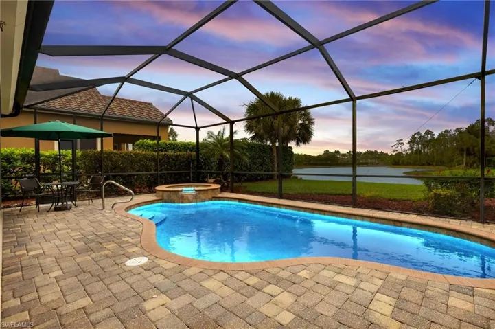 Pool at dusk with glass enclosure, a patio, a water view, and a pool with connected hot tub