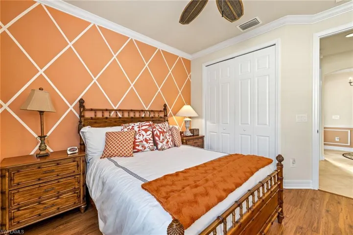 Bedroom with wood finished floors, visible vents, arched walkways, ornamental molding, and a closet
