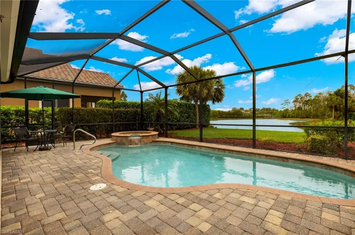 View of swimming pool featuring a patio area, glass enclosure, a pool with connected hot tub, and a water view