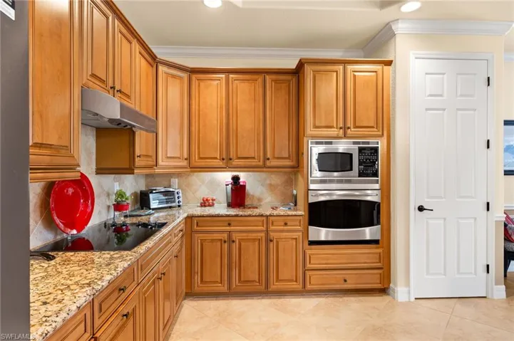 Kitchen with under cabinet range hood, stainless steel appliances, crown molding, and light stone counters