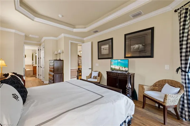 Bedroom with a raised ceiling, wood finished floors, visible vents, and ornamental molding