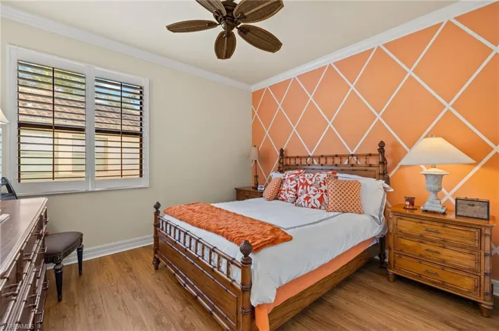 Bedroom with wood finished floors, baseboards, ceiling fan, ornamental molding, and an accent wall
