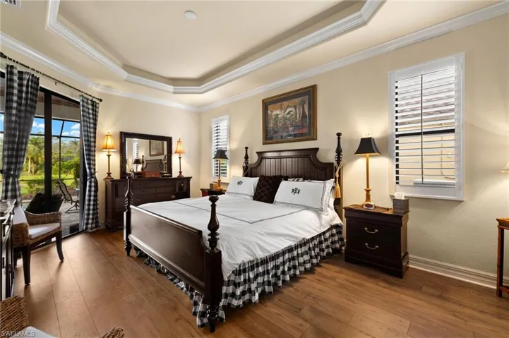 Bedroom with baseboards, a tray ceiling, hardwood / wood-style flooring, crown molding, and access to outside
