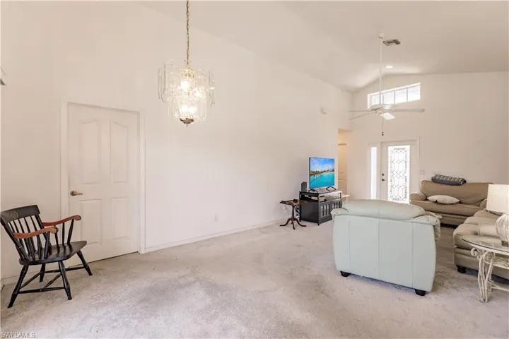 Living room featuring ceiling fan with notable chandelier, light carpet, and high vaulted ceiling