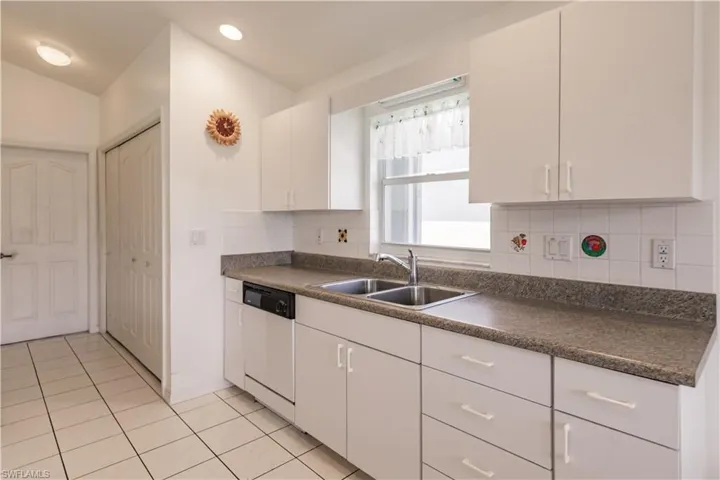 Kitchen featuring sink, backsplash, white cabinetry, light tile patterned flooring, and dishwasher