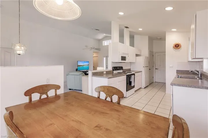 Tiled dining space featuring high vaulted ceiling, sink, and ceiling fan with notable chandelier