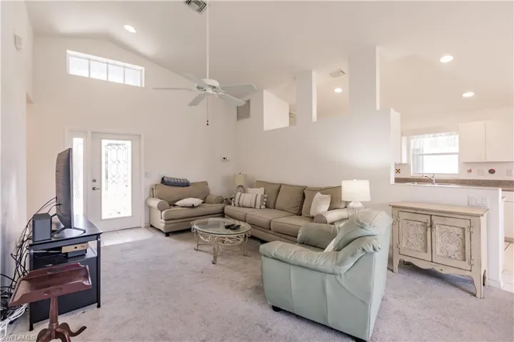 Carpeted living room with high vaulted ceiling, sink, and ceiling fan