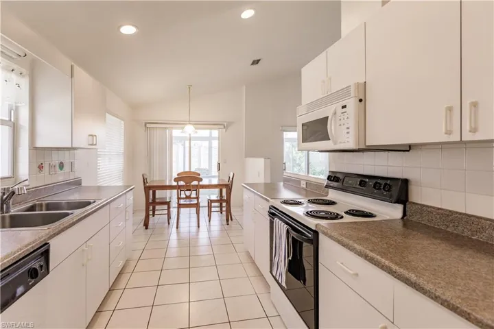Kitchen with white cabinets, lofted ceiling, decorative backsplash, and white appliances