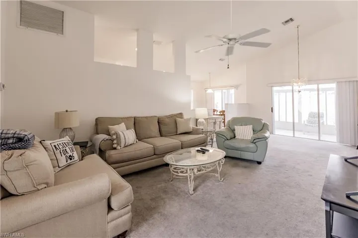 Carpeted living room featuring ceiling fan with notable chandelier and high vaulted ceiling