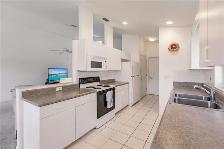 Kitchen with sink, white appliances, backsplash, and light colored carpet