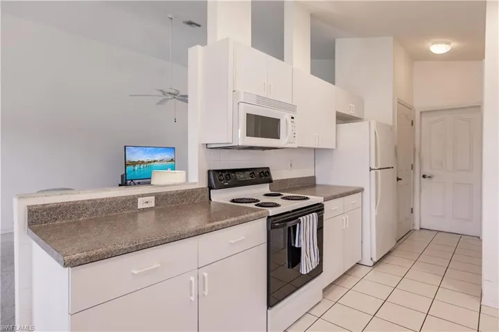 Kitchen featuring white appliances, light tile patterned floors, decorative backsplash, white cabinetry, and ceiling fan
