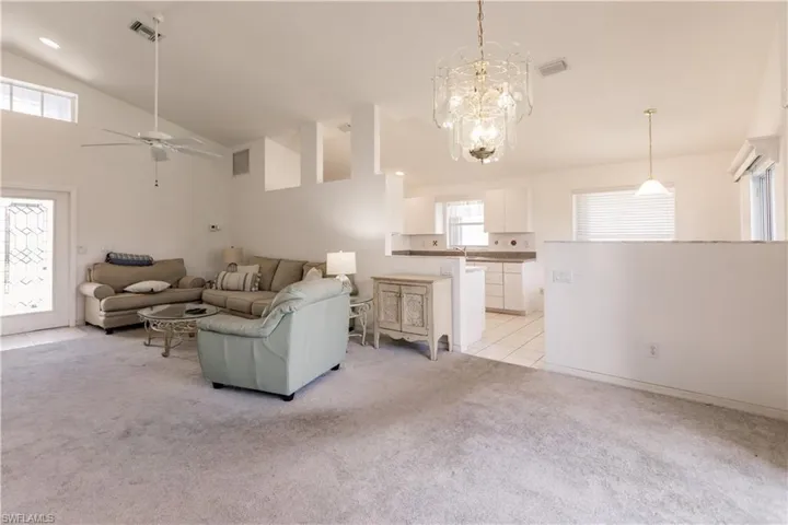 Unfurnished living room with light tile patterned flooring, ceiling fan with notable chandelier, and high vaulted ceiling