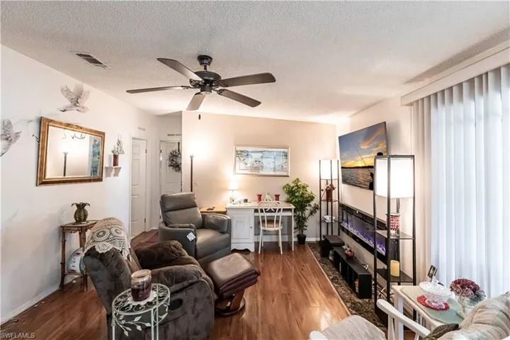 Living area featuring a textured ceiling, visible vents, baseboards, dark wood finished floors, and a ceiling fan