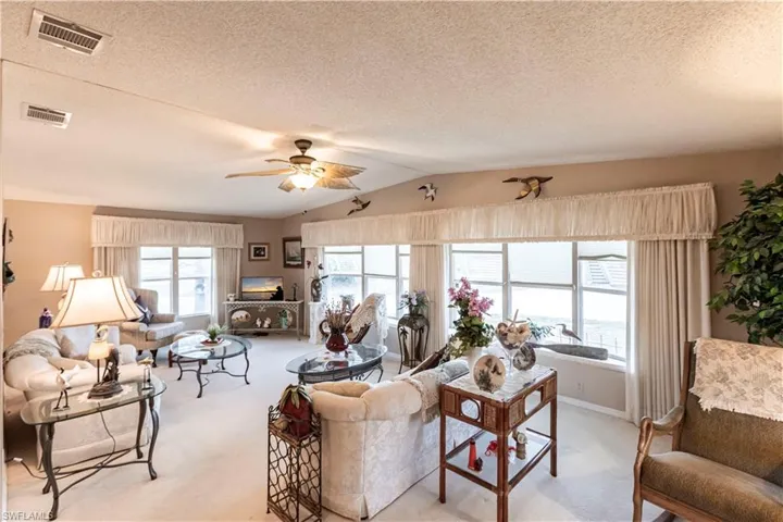 Living room featuring light colored carpet, visible vents, ceiling fan, and vaulted ceiling