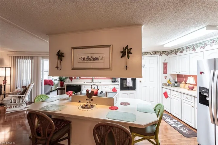 Kitchen with a textured ceiling, white cabinetry, a breakfast bar area, black appliances, and light wood-type flooring