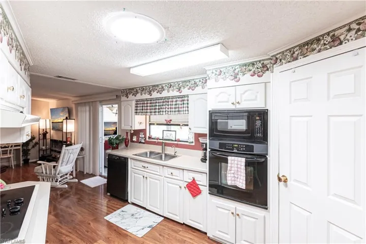 Kitchen featuring a textured ceiling, a sink, light countertops, black appliances, and wood finished floors
