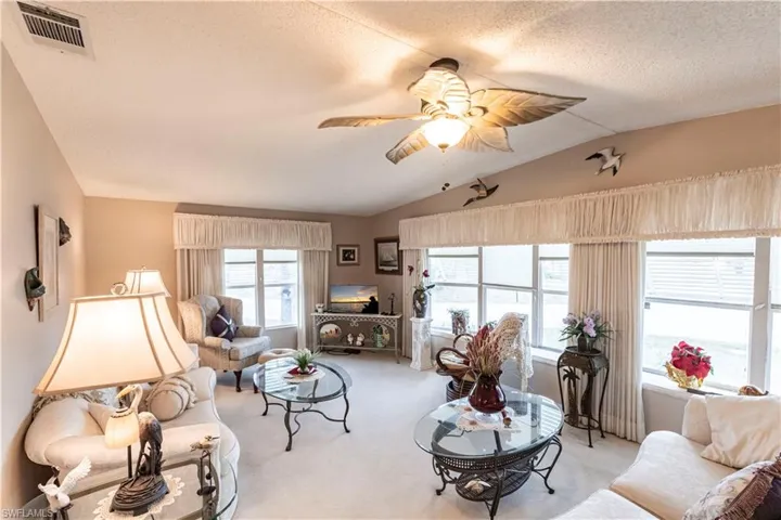 Carpeted living room with a textured ceiling, visible vents, ceiling fan, and vaulted ceiling