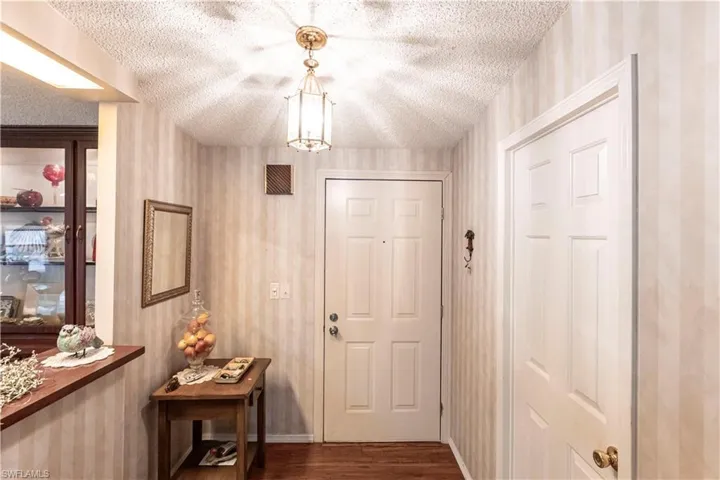 Entryway featuring dark wood-style floors, a textured ceiling, wallpapered walls, and baseboards