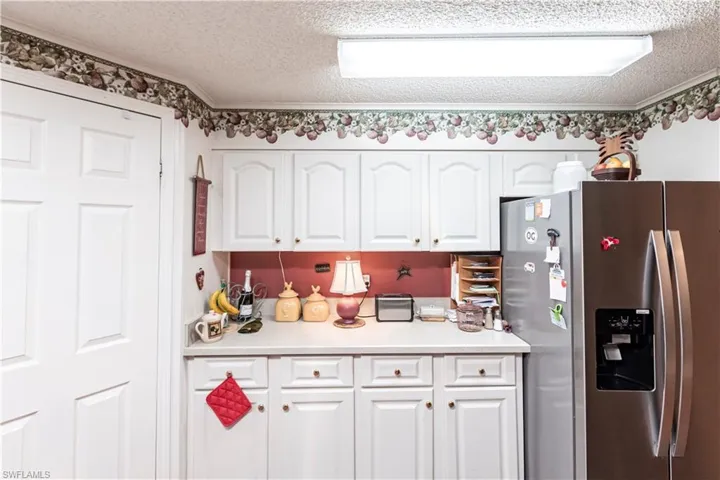 Kitchen with a textured ceiling, light countertops, white cabinets, and stainless steel fridge with ice dispenser