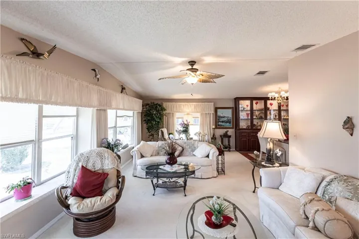 Carpeted living area featuring visible vents, a ceiling fan, a textured ceiling, and vaulted ceiling