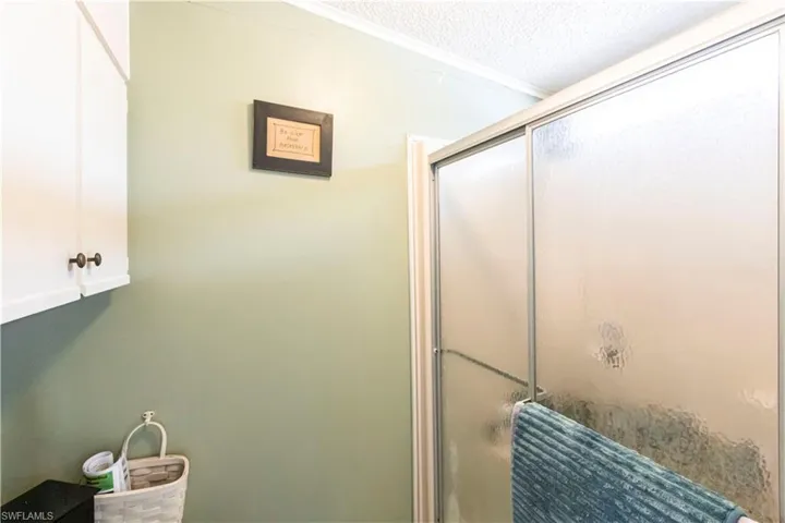 Full bath with a textured ceiling, a shower with shower door, and ornamental molding