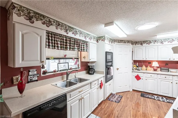 Kitchen featuring a sink, light wood-type flooring, black appliances, white cabinetry, and a textured ceiling