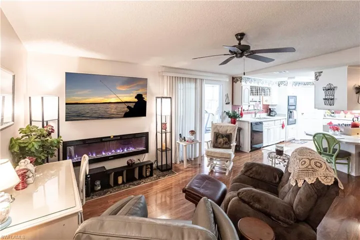 Living area featuring ceiling fan, light wood-style floors, a textured ceiling, and a glass covered fireplace
