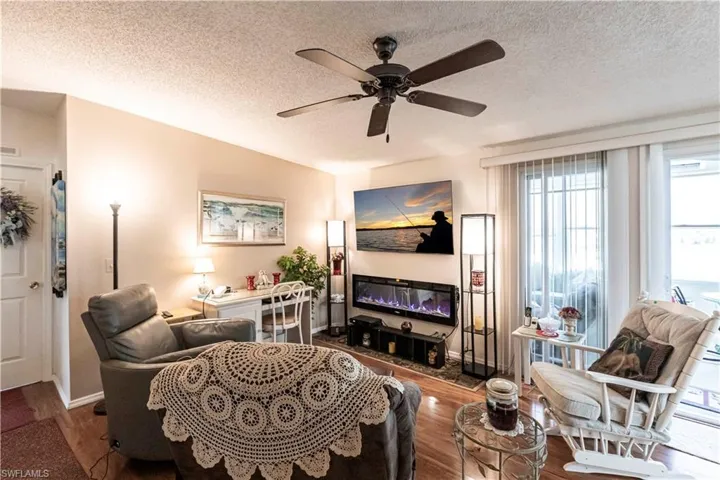 Living room with a textured ceiling, ceiling fan, visible vents, baseboards, and wood finished floors