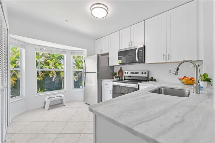 Kitchen featuring light stone countertops, baseboards, white cabinetry, a sink, and stainless steel appliances