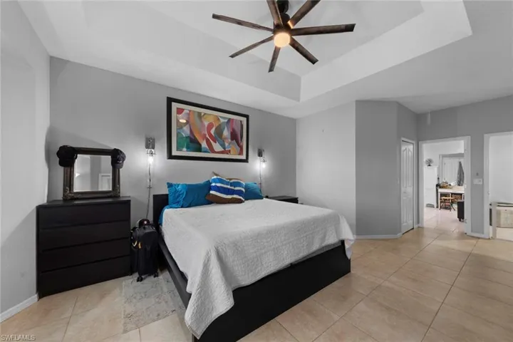 Bedroom with light tile patterned floors, a tray ceiling, ceiling fan, and ensuite bathroom