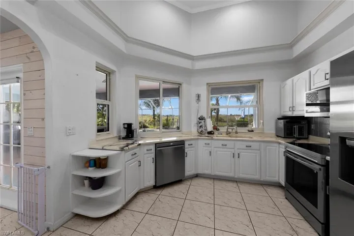 Kitchen featuring white cabinets, appliances with stainless steel finishes, a towering ceiling, and ornamental molding