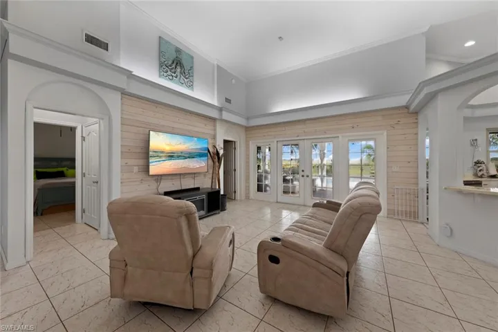 Living room featuring wood walls, light tile patterned floors, ornamental molding, a high ceiling, and french doors