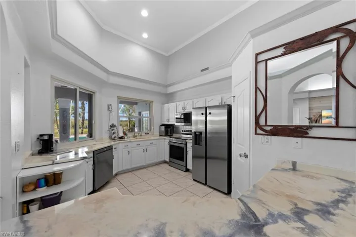 Kitchen with crown molding, light tile patterned flooring, stainless steel appliances, and white cabinets