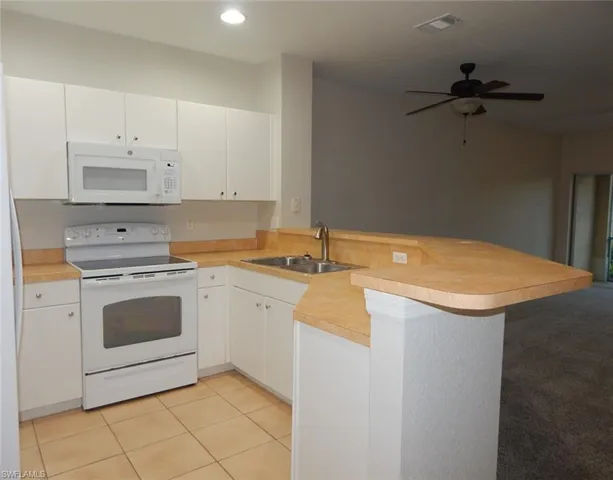 Kitchen with a peninsula, white appliances, white cabinets, light countertops, and light tile patterned floors