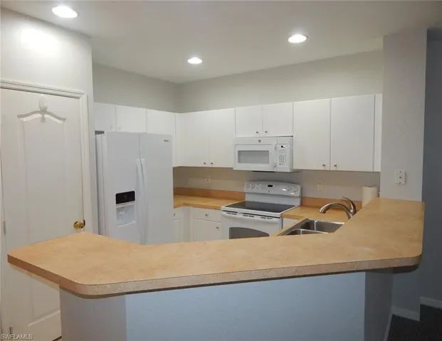 Kitchen featuring white appliances, white cabinetry, light countertops, recessed lighting, and a peninsula