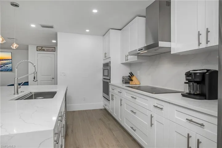 Kitchen with wall chimney range hood, light stone countertops, pendant lighting, light wood-type flooring, and recessed lighting