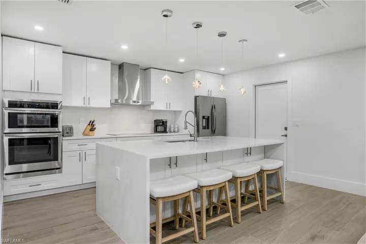 Kitchen featuring wood tiled floors, a kitchen bar, decorative light fixtures, light stone countertops, and recessed lighting
