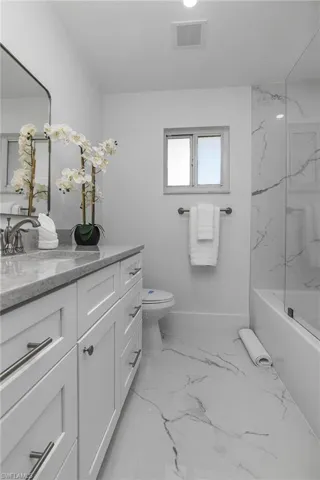 Full bathroom with vanity, a combined bath / shower with marble appearance, and light marble finish flooring