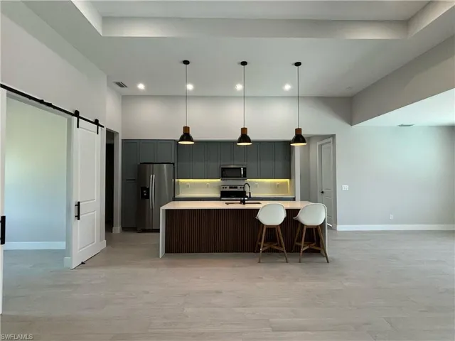 Kitchen with a barn door, stainless steel appliances, a kitchen island with sink, and pendant lighting