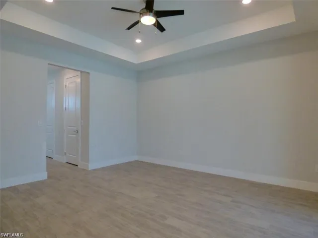 Spare room with ceiling fan, a raised ceiling, and light hardwood / wood-style flooring