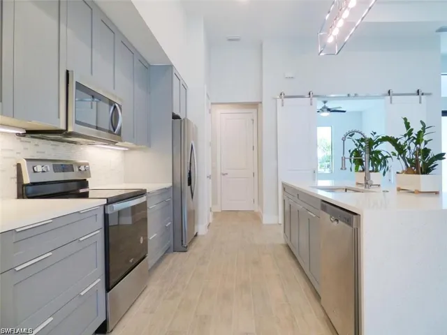 Kitchen featuring ceiling fan, light hardwood / wood-style flooring, stainless steel appliances, gray cabinets, and backsplash