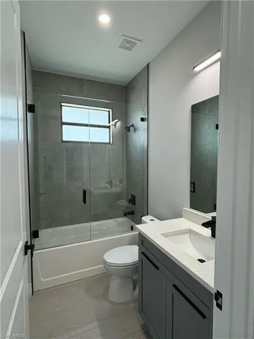 Full bathroom with oversized vanity, tile floors, toilet, and bath / shower combo with glass door