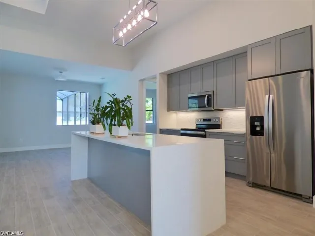 Kitchen with light wood-type flooring, a kitchen island, gray cabinetry, appliances with stainless steel finishes, and backsplash